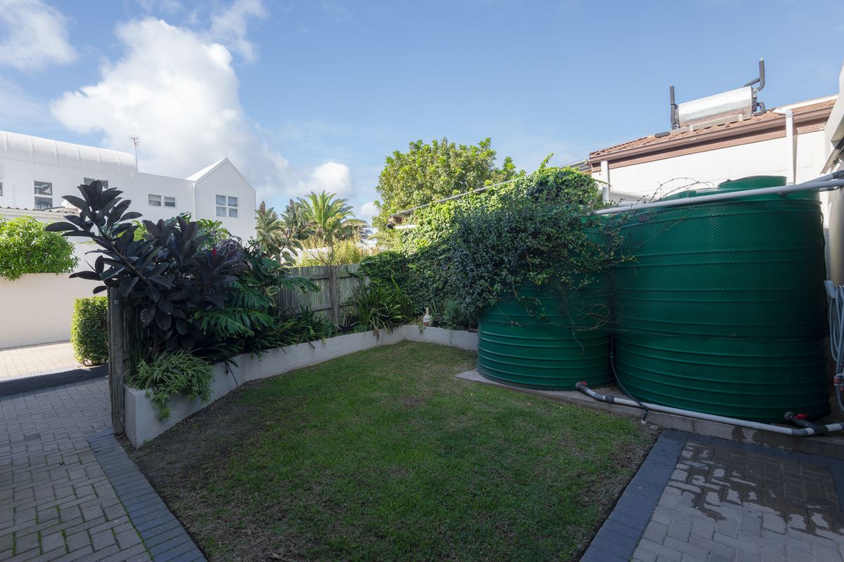 A private rear garden area featuring a small lawn, perimeter fencing, and two large green water storage tanks.