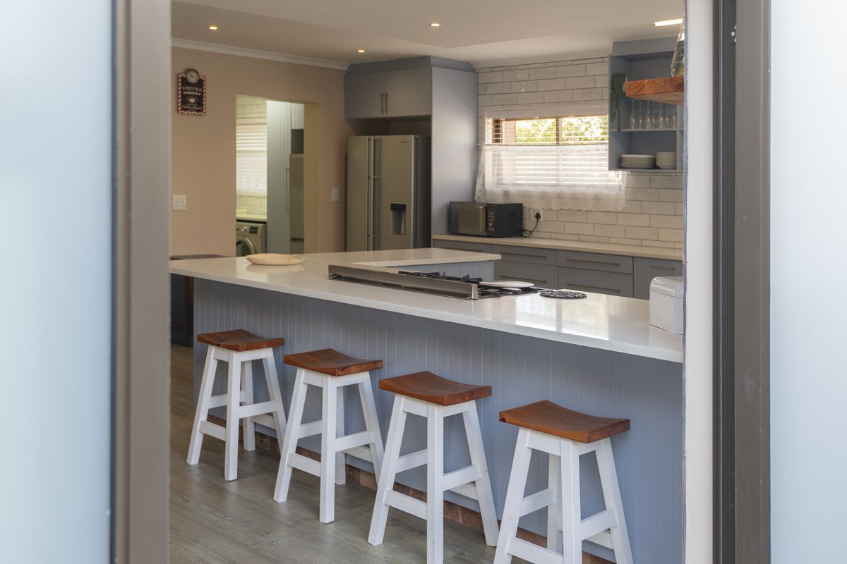 Modern kitchen featuring a large breakfast bar with integrated gas hob, subway tile backsplash, and ample cabinetry, leading into a separate laundry area.