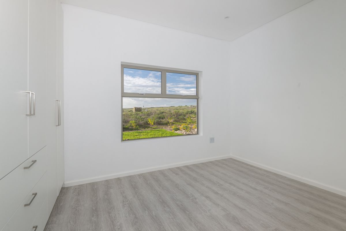 A bright, modern bedroom featuring light wood-look flooring, built-in white cabinetry, and a window offering scenic natural views.