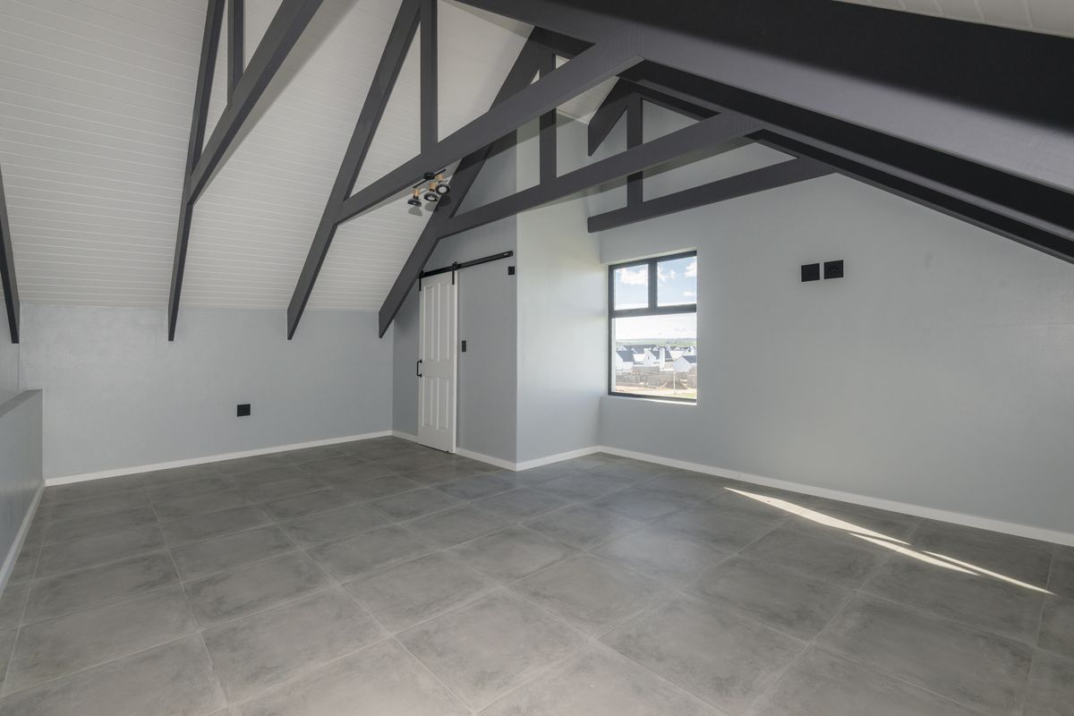Spacious attic-style bedroom featuring exposed dark timber rafters, vaulted ceilings, large format grey floor tiles, and a sliding barn-style door.