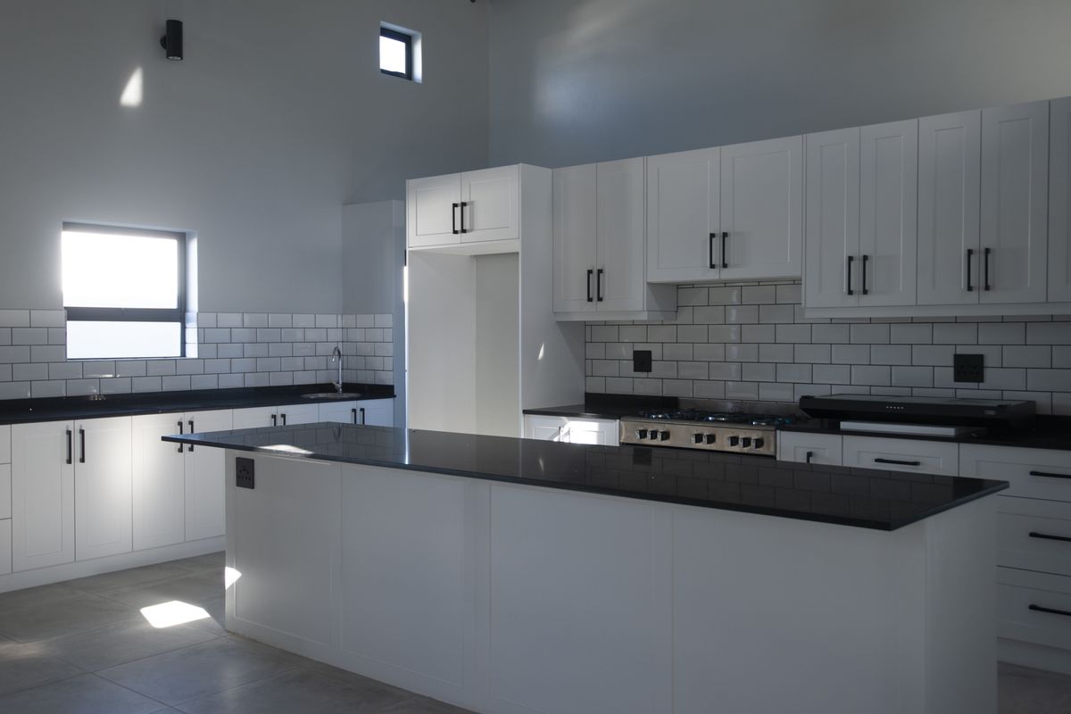 Modern kitchen featuring white shaker-style cabinetry, contrasting black countertops, subway tile backsplash, and a central island with integrated gas cooktop.