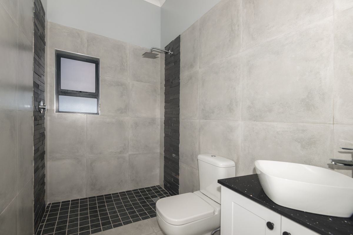 Modern bathroom featuring a walk-in shower with rainfall showerhead, contemporary vanity with vessel sink, and sleek grey tiled walls with stone accents.