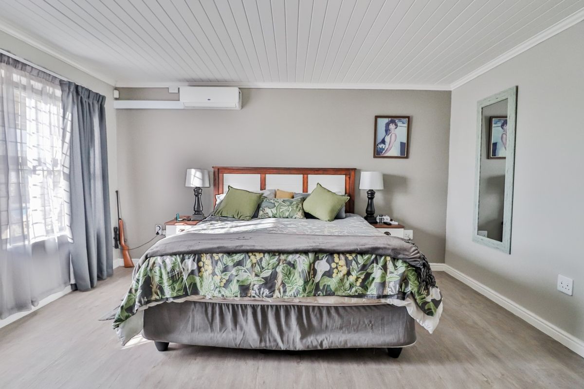 A well-maintained bedroom featuring light-toned laminate flooring, a tongue-and-groove ceiling, and a wall-mounted air conditioning unit.
