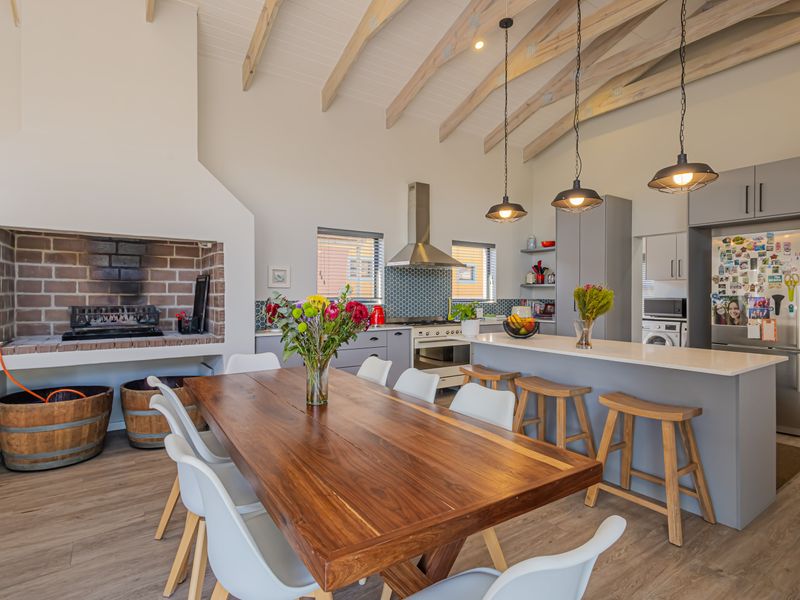 Spacious open-plan living area featuring a vaulted ceiling with exposed rafters, a built-in brick fireplace, and a modern kitchen with a central island.