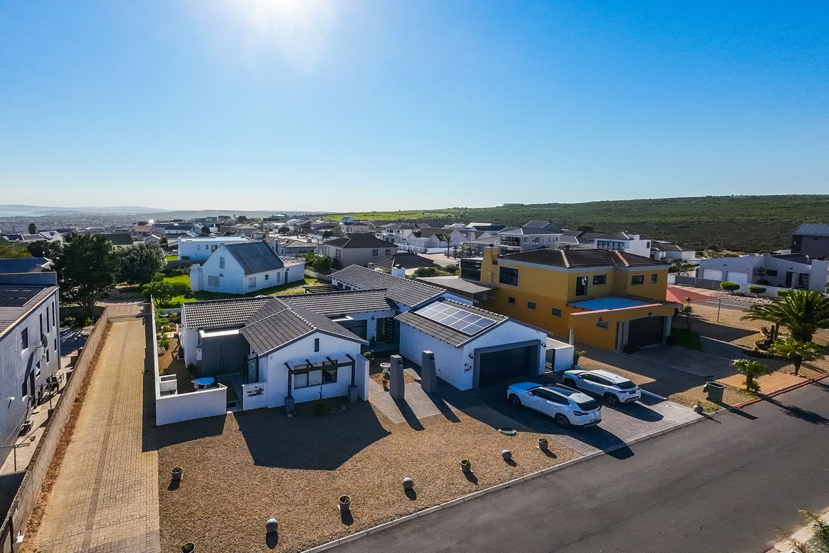 Aerial view of a residential property featuring a tiled roof with solar panels, a paved driveway, and a garage in a coastal neighborhood.