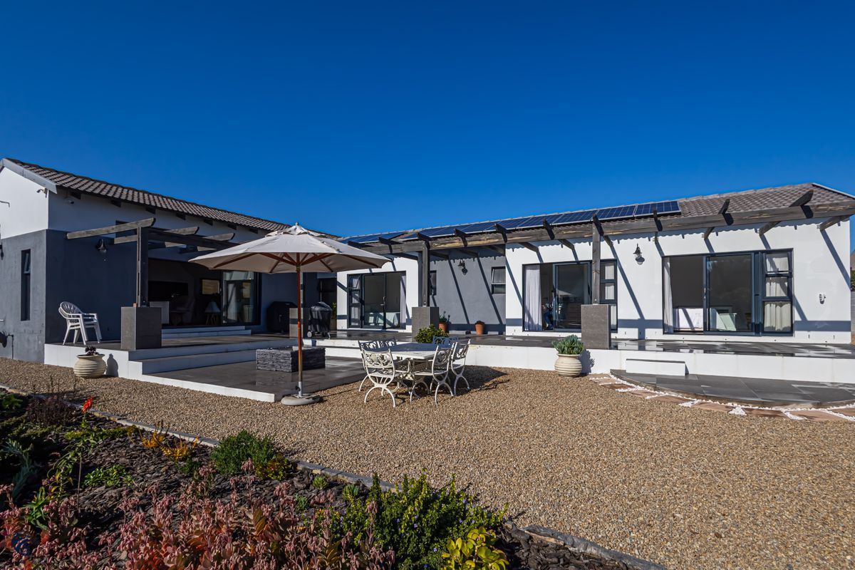 Spacious rear exterior featuring a large tiled patio with timber pergola, solar panels on the roof, and direct access via sliding glass doors.
