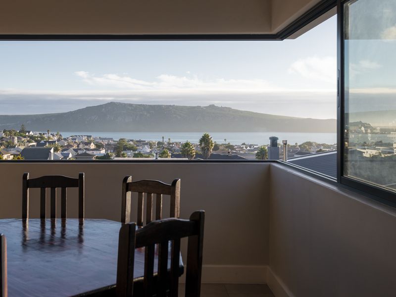 A bright interior space featuring a large corner window that offers expansive, panoramic views of the coastal town, bay, and distant mountains.