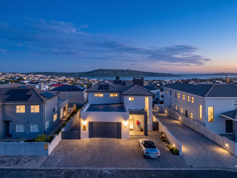 Aerial view of a modern two-story residential property featuring a paved driveway, solar panels, and a tiled roof at twilight.