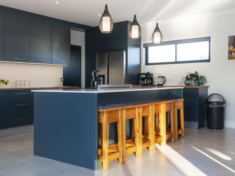 Modern kitchen featuring dark blue cabinetry, a central island with stone countertops, pendant lighting, and tiled flooring.