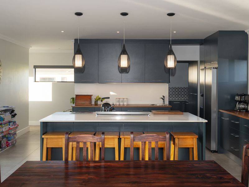 Modern kitchen featuring dark blue cabinetry, a central island with quartz countertops, pendant lighting, and integrated appliances.