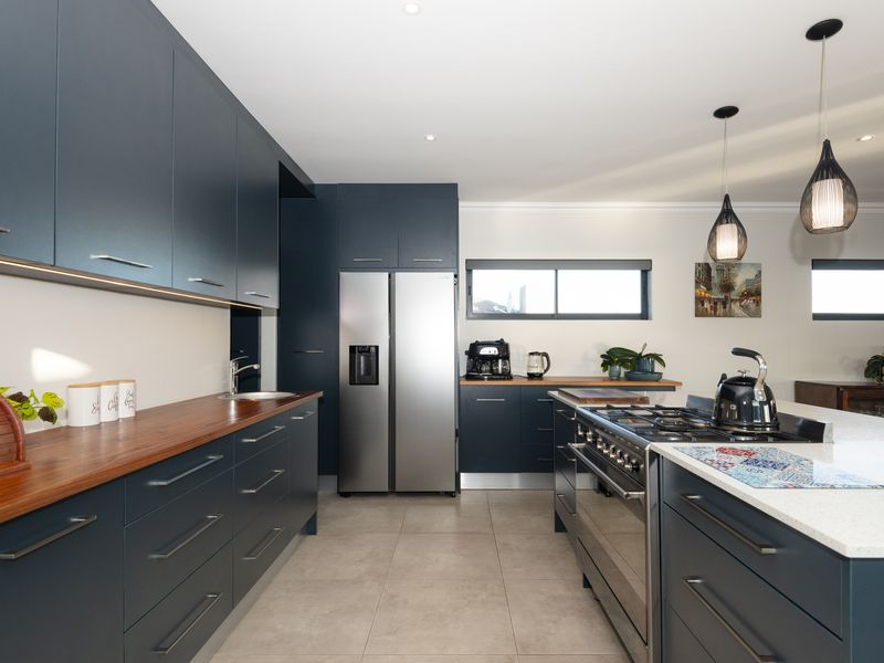 Modern kitchen featuring dark blue cabinetry, wooden and stone countertops, a large gas range cooker, and high-quality integrated appliances.