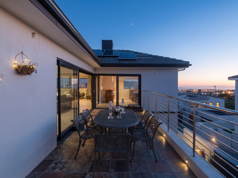 A spacious covered balcony featuring decorative tiled flooring, stainless steel balustrades, and recessed lighting, offering expansive sunset views.