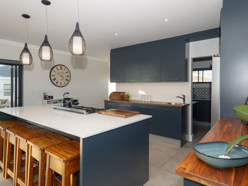 Modern kitchen featuring a large island with quartz countertops, gas cooktop, dark blue cabinetry, and contrasting wooden work surfaces with integrated sink.