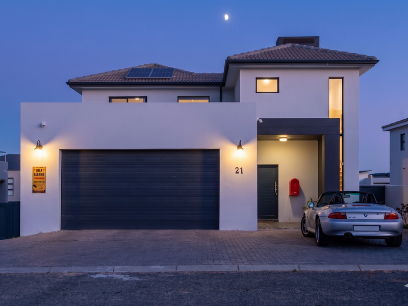 Modern double-story residential facade featuring a paved driveway, integrated garage, solar panels, and contemporary exterior lighting at dusk.