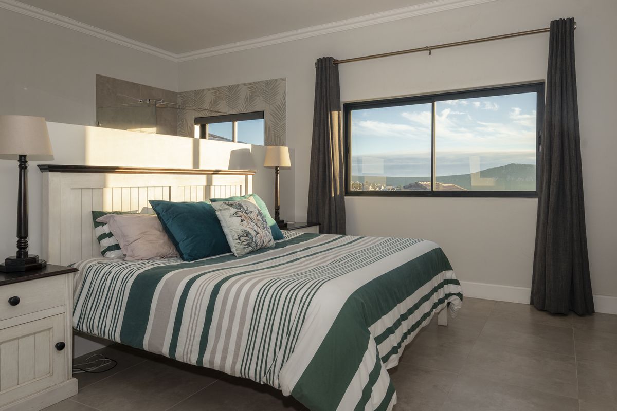 Spacious bedroom featuring tiled flooring, a large sliding window with scenic views, and an open-plan en-suite bathroom with a glass shower enclosure.