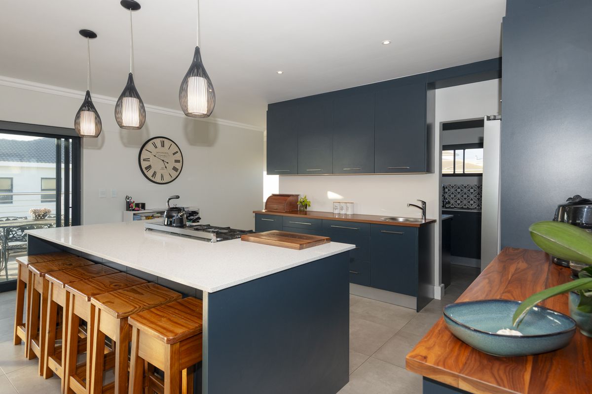 Modern kitchen featuring a large island with quartz countertops, gas cooktop, dark blue cabinetry, and contrasting wooden work surfaces with integrated sink.