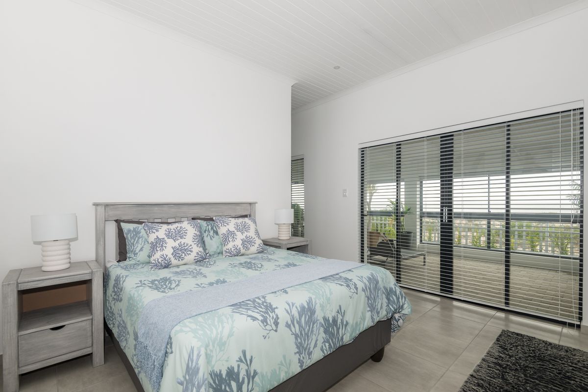 Spacious bedroom featuring neutral tiled flooring, high ceilings, and large sliding glass doors providing direct access to an outdoor balcony area.