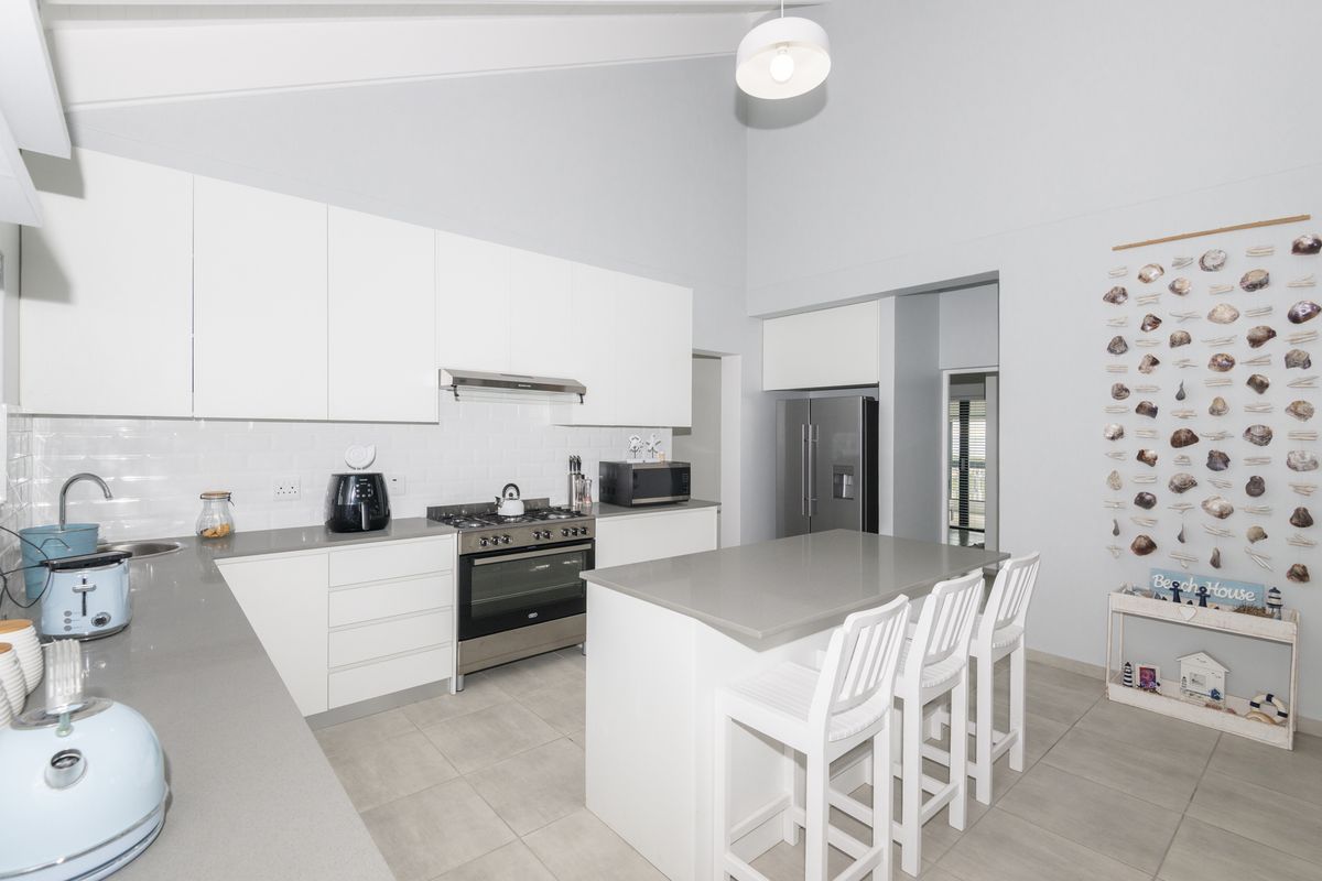 Modern kitchen featuring white cabinetry, stone countertops, a central island, and high vaulted ceilings with integrated lighting.