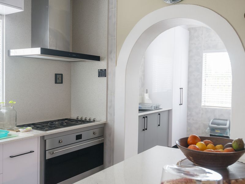 A functional kitchen featuring a gas cooktop, built-in oven, extractor fan, and stone countertops, connected to a secondary prep area through a classic archway.