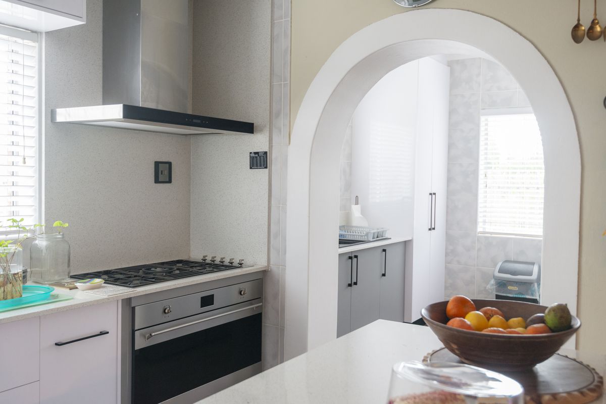 A functional kitchen featuring a gas cooktop, built-in oven, extractor fan, and stone countertops, connected to a secondary prep area through a classic archway.