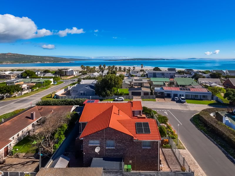 Aerial view of the property featuring a brick exterior, tiled roof with solar panels, and proximity to the coastal landscape.
