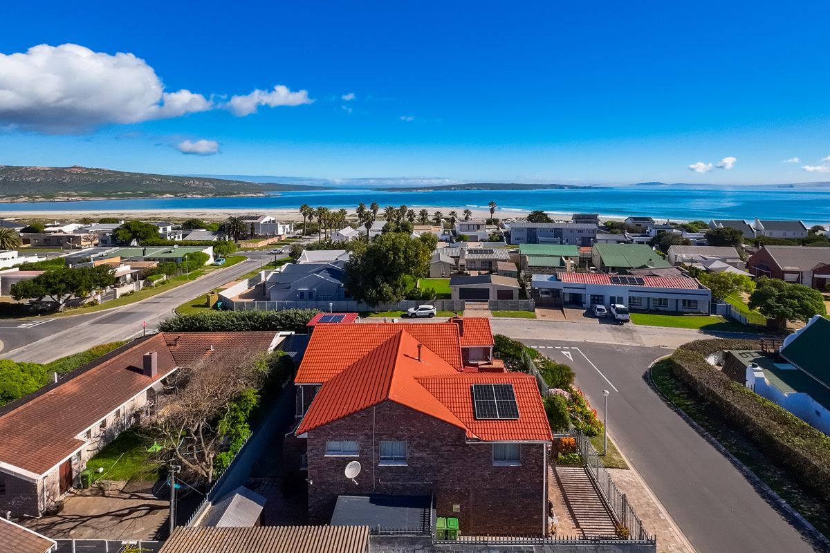 Aerial view of the property featuring a brick exterior, tiled roof with solar panels, and proximity to the coastal landscape.