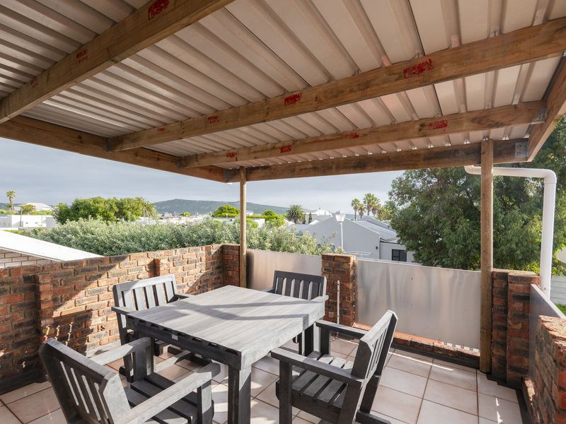 An elevated outdoor balcony featuring a timber-framed corrugated roof, face brick walls, and tiled flooring, offering pleasant neighbourhood views.