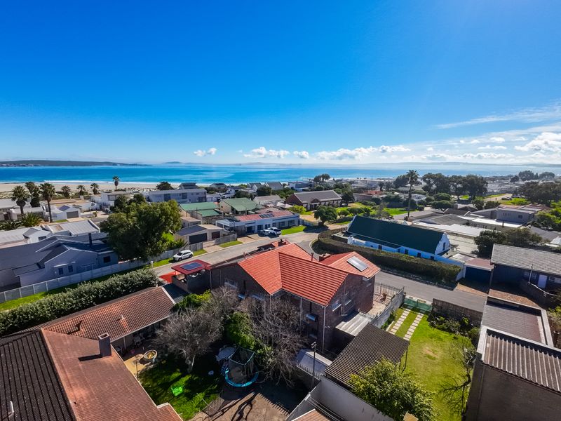 Aerial view of the property showcasing its location, roof structure, and proximity to the coastline and surrounding neighborhood.