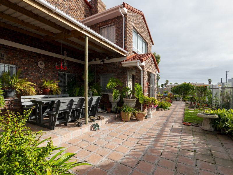 A spacious covered patio featuring terracotta tile flooring and exposed brick walls, providing a comfortable outdoor living area overlooking the garden.