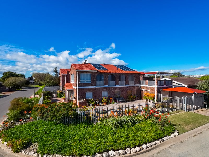 Aerial view of a two-story brick residential property featuring a tiled roof with solar panels, a fenced garden, and a carport.