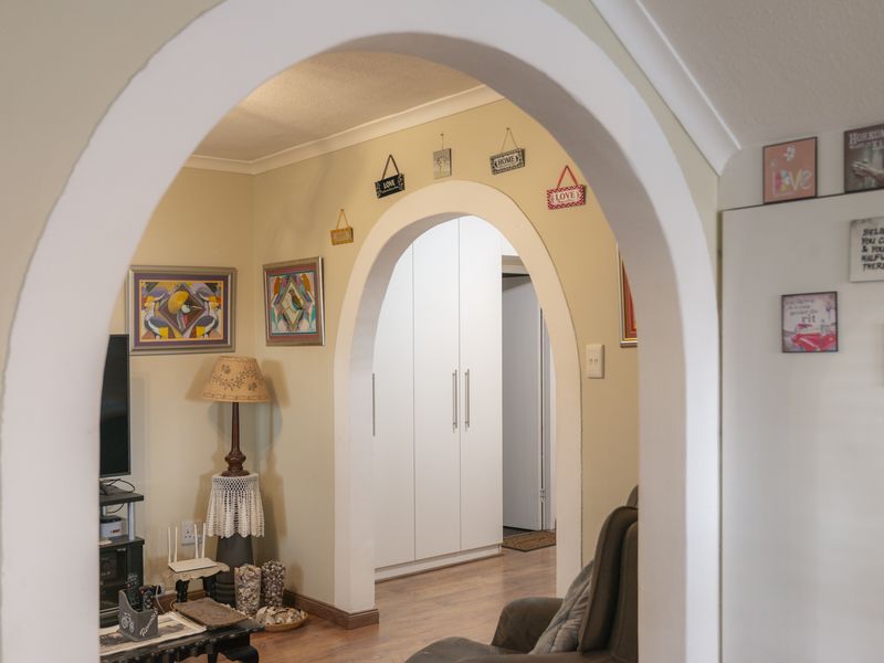 A living area featuring a distinctive arched doorway leading to a hallway with built-in storage cupboards and laminate flooring throughout.