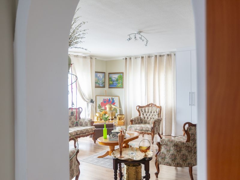 A bright living room featuring laminate flooring, a built-in wardrobe, and a classic archway entrance, offering a comfortable and well-lit living space.