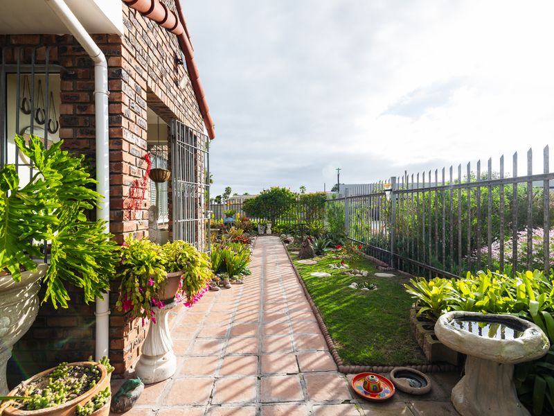 A well-maintained rear garden area featuring a brick facade, paved walkway, and secure metal fencing.