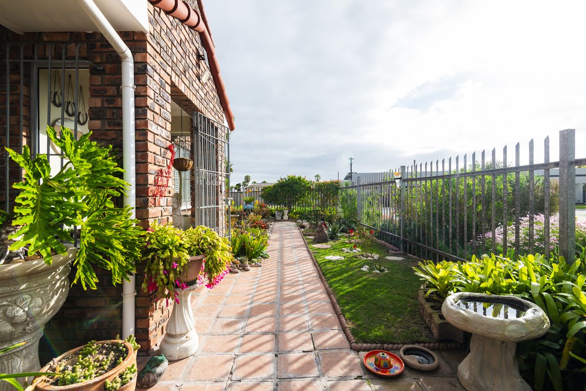 A well-maintained rear garden area featuring a brick facade, paved walkway, and secure metal fencing.