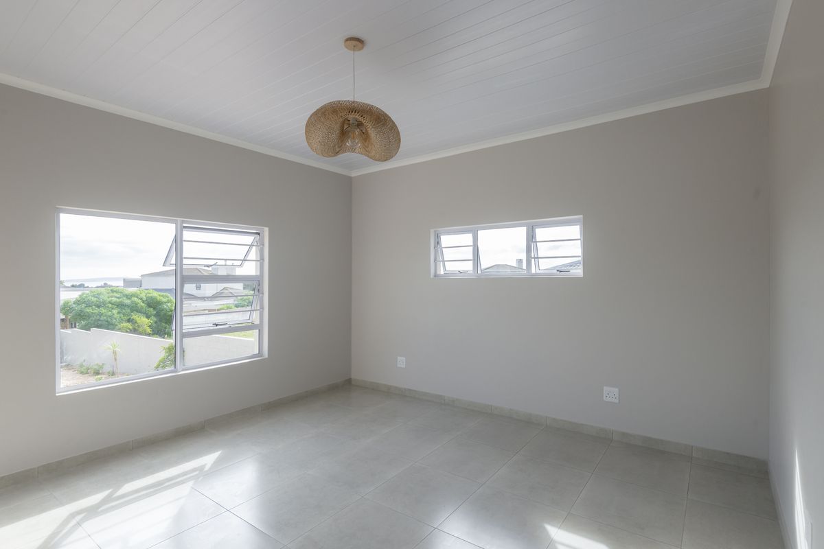 A bright, empty bedroom featuring neutral walls, tiled flooring, and large louvre windows that provide ample natural light.