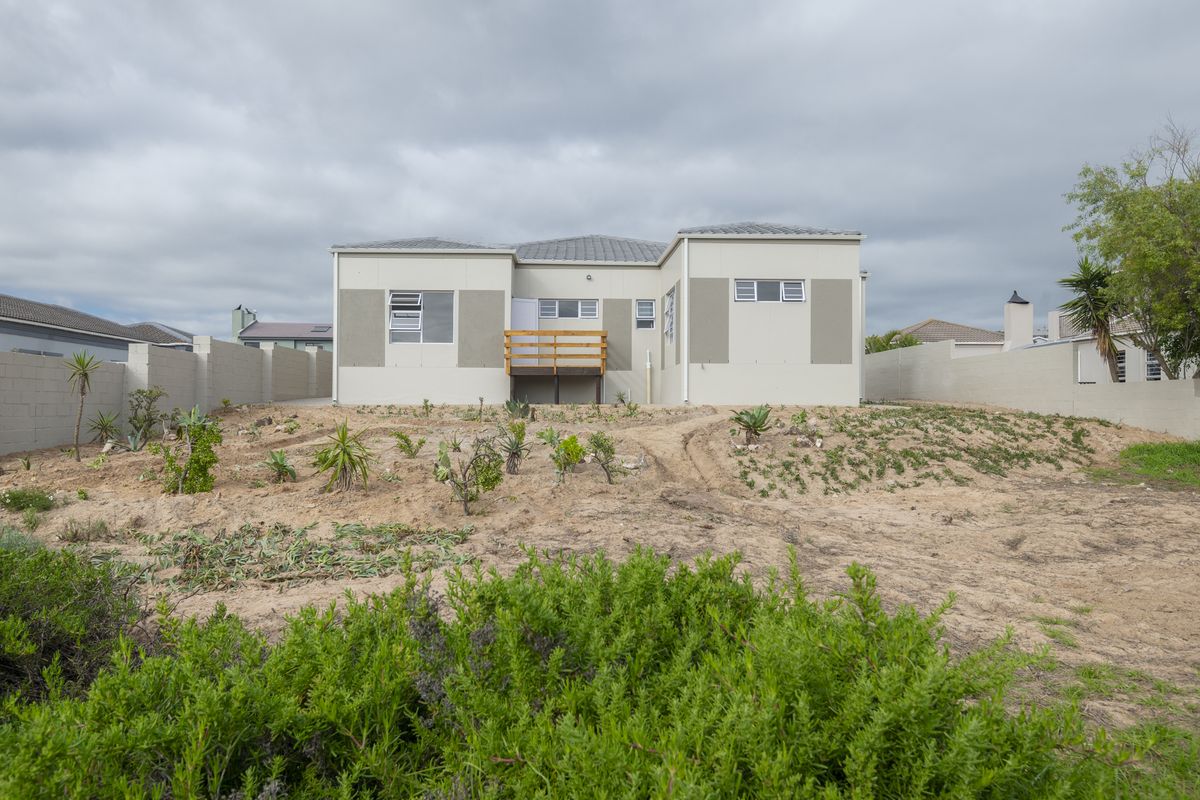 Rear view of a modern single-story house featuring a timber deck, tiled roof, and a large, undeveloped garden area enclosed by boundary walls.