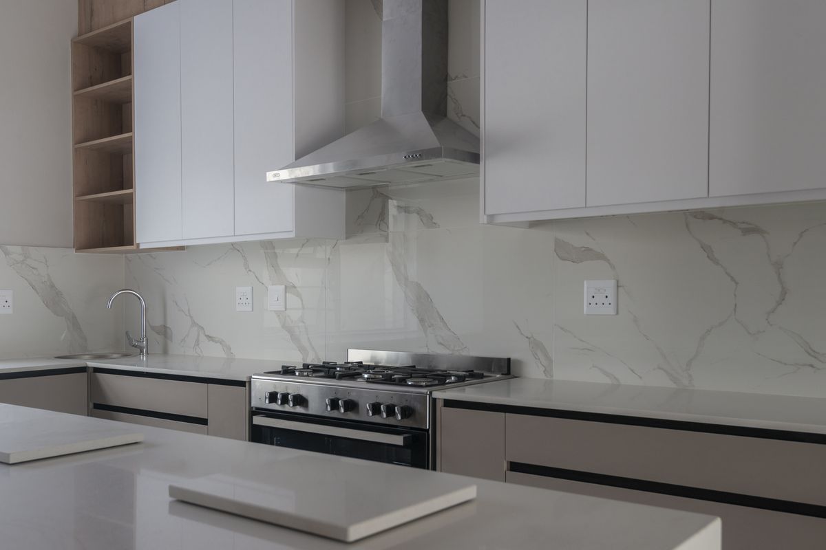 Modern kitchen featuring sleek white cabinetry, marble-look splashback, quartz countertops, and a stainless steel gas stove with an integrated extractor fan.
