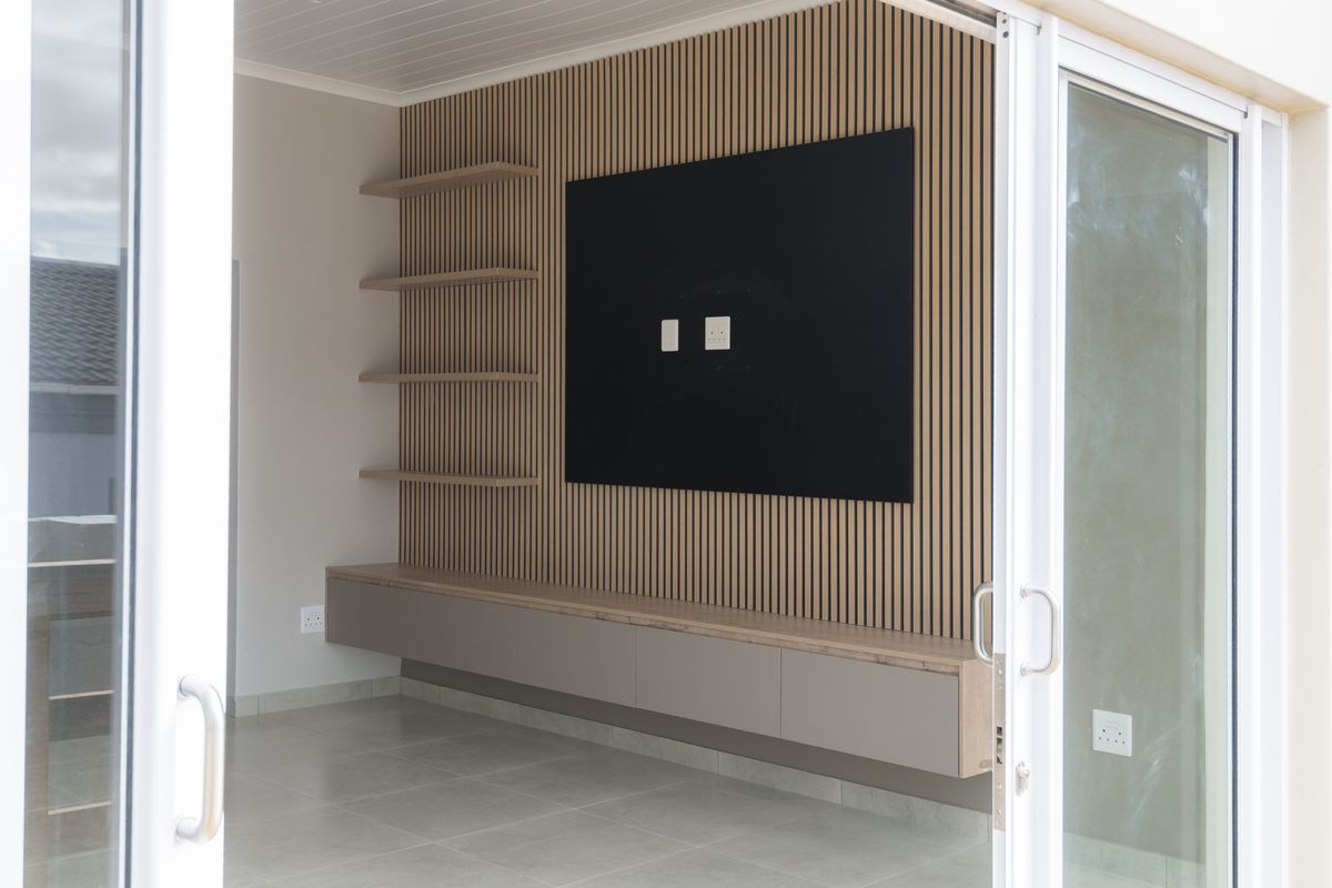 Modern living area featuring a contemporary slatted timber feature wall with integrated floating cabinetry, shelving, and large sliding glass doors for natural light.