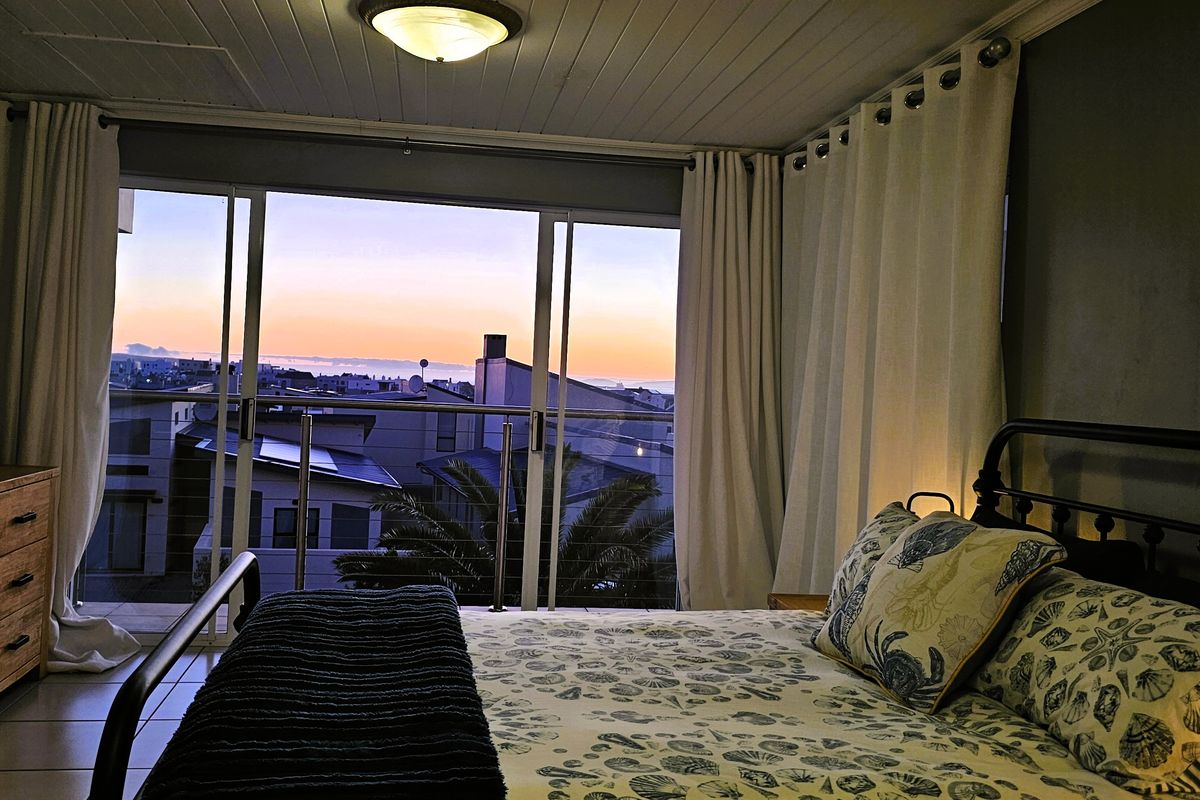 A cozy bedroom featuring tiled flooring, a tongue and groove ceiling, and large sliding glass doors that open onto a balcony with sunset views.