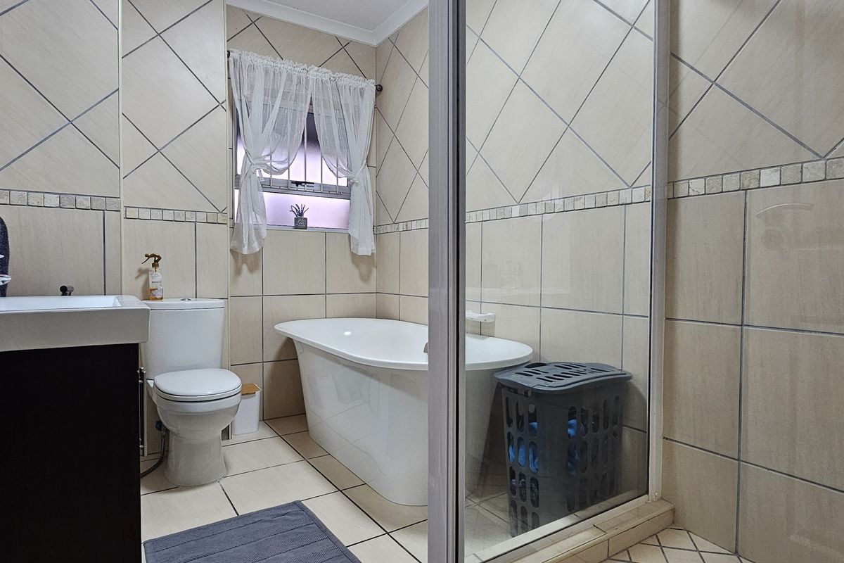 A well-maintained bathroom featuring a freestanding bathtub, a separate glass-enclosed shower, a vanity basin, and neutral ceramic tiling throughout.