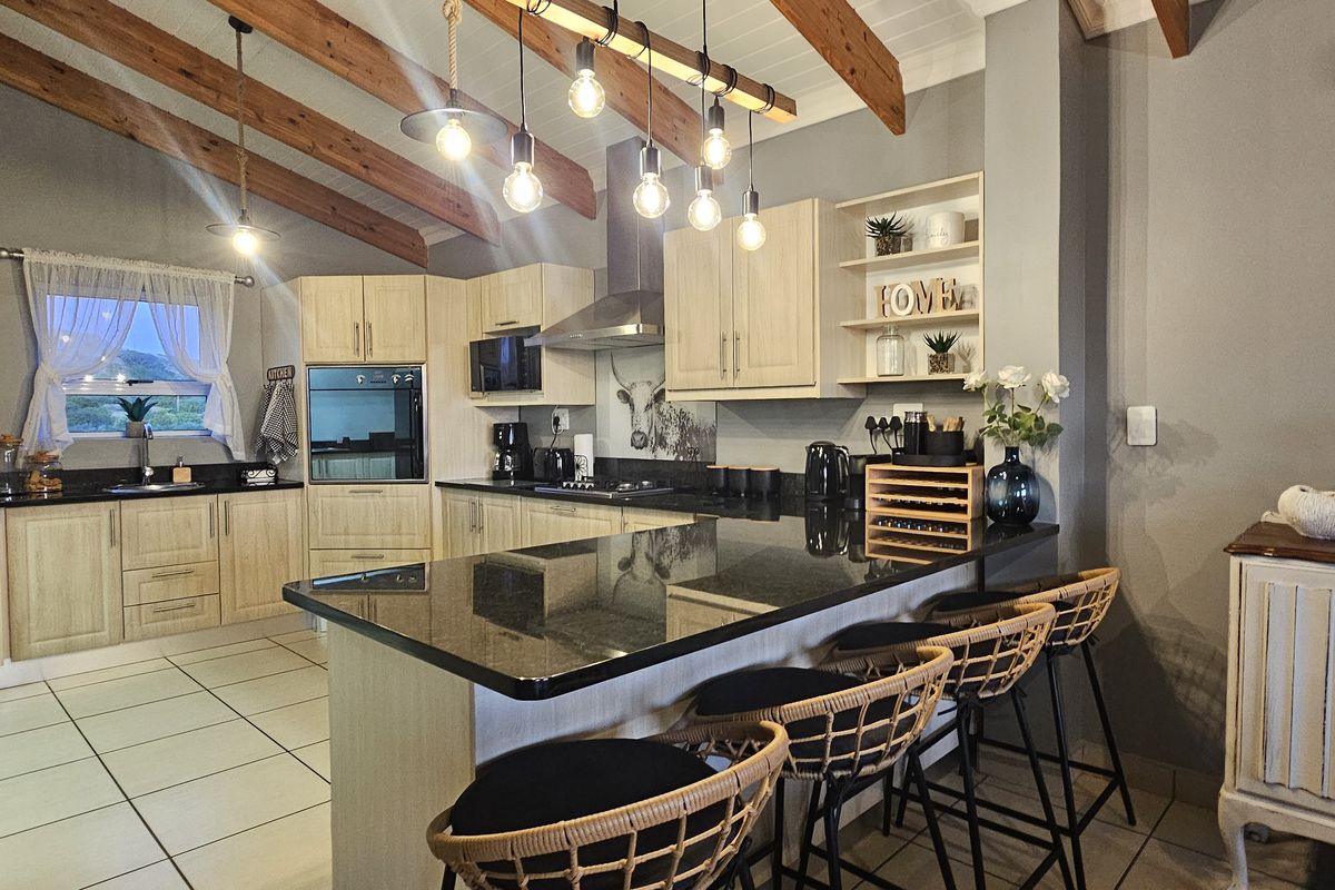 Modern kitchen featuring light wood cabinetry, granite countertops, a central island, and exposed timber beams under a vaulted ceiling.