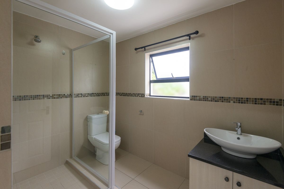 A clean, modern bathroom featuring a glass-enclosed shower, a vessel sink vanity with granite countertop, and neutral wall tiling.
