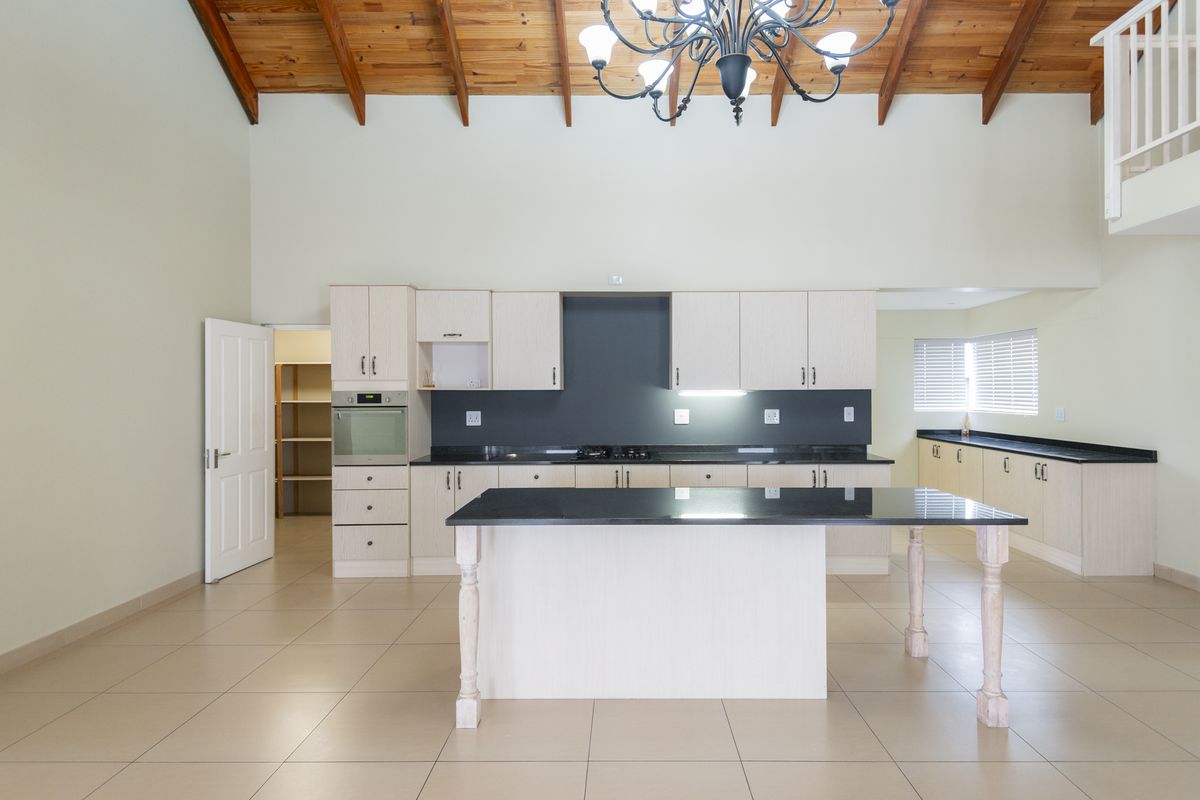 Spacious kitchen featuring light wood cabinetry, granite countertops, a central island, and a walk-in pantry, set under a high vaulted timber ceiling.