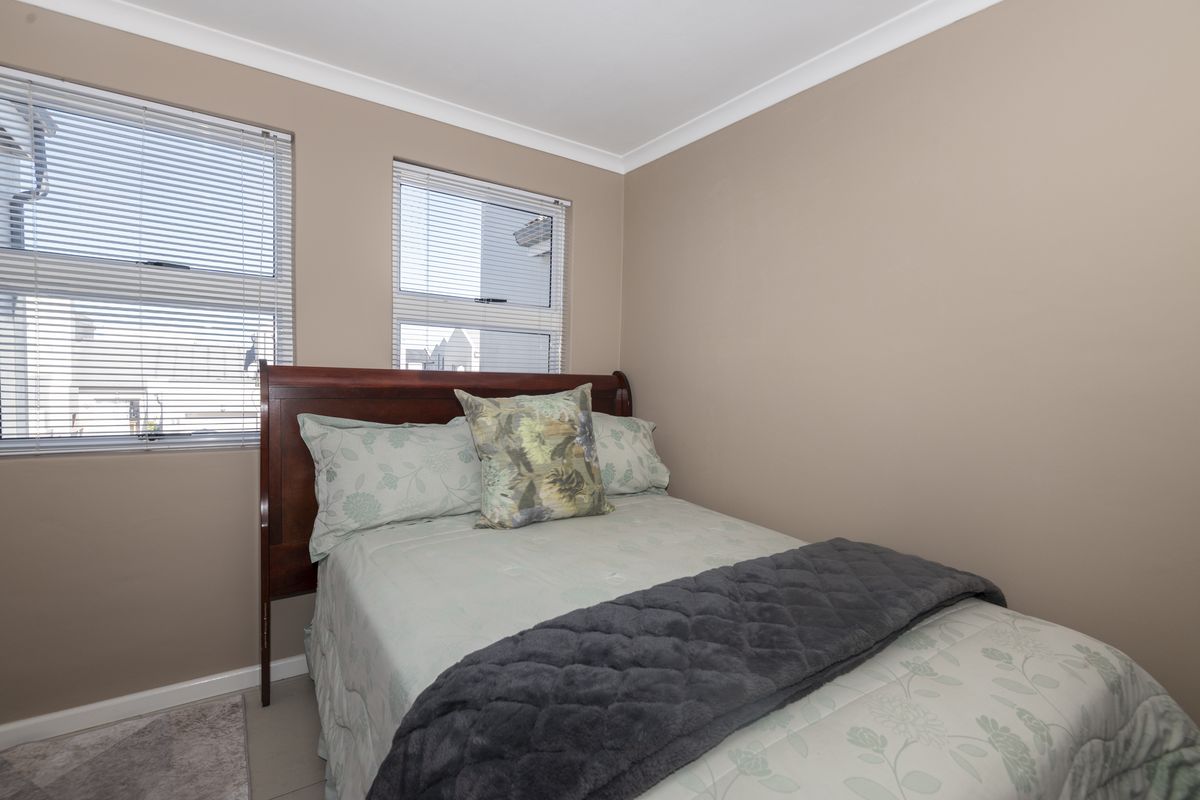 A compact bedroom featuring neutral wall tones, tiled flooring, and two windows fitted with horizontal blinds.
