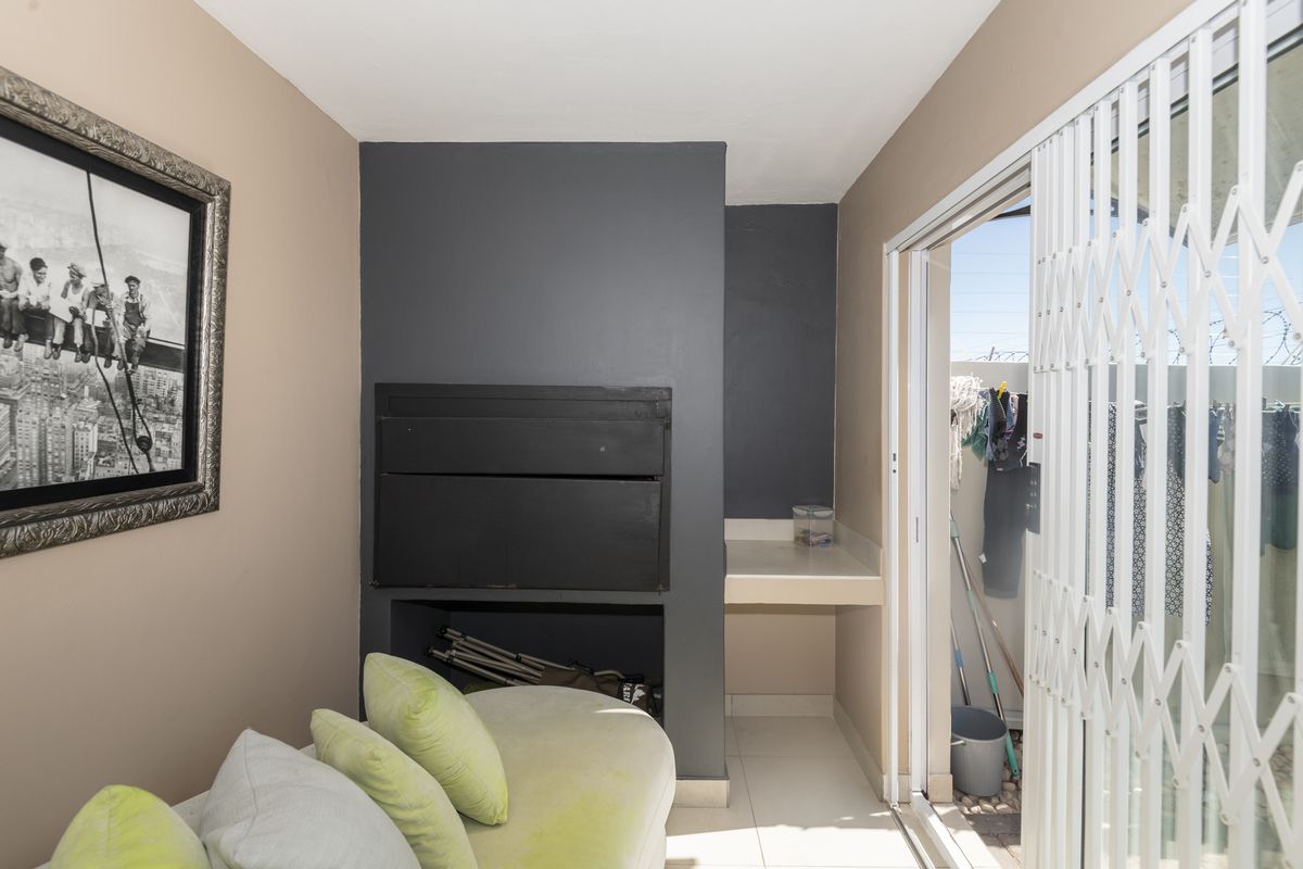 Indoor entertainment area featuring a built-in braai and tiled flooring, with direct access to an outdoor space through a sliding security gate.