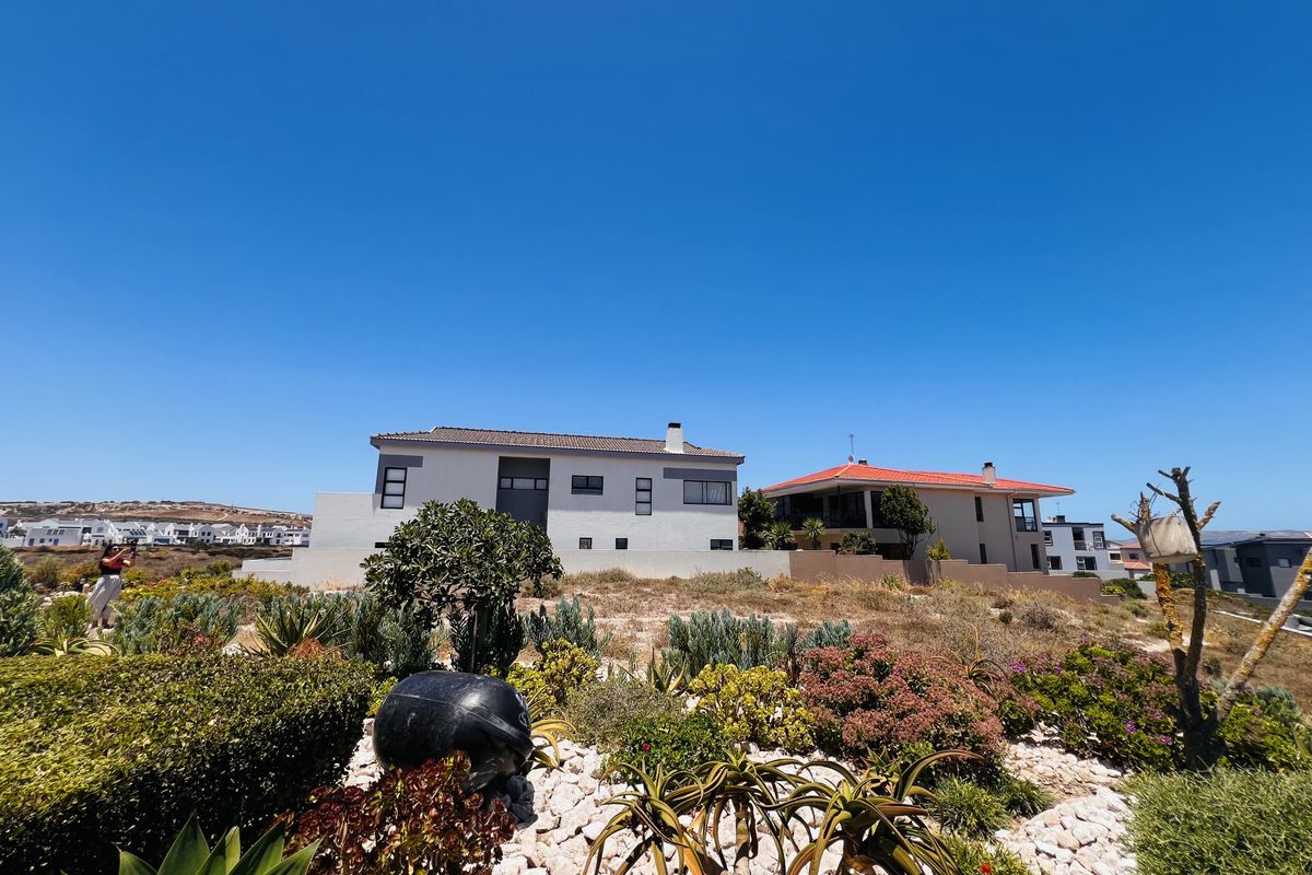 A view of a residential property featuring landscaped garden beds with indigenous plants and a clear view of the neighboring house exterior.