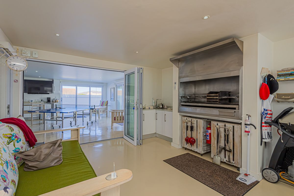 An indoor entertainment area featuring a built-in stainless steel braai, recessed lighting, and bi-fold doors opening to an adjacent sunroom.