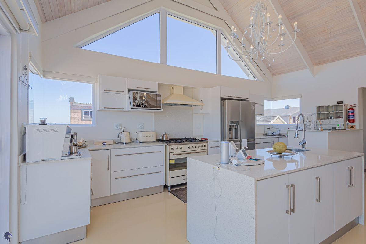 Modern open-plan kitchen featuring white cabinetry, stone countertops, a central island, and a high vaulted ceiling with large windows for natural light.