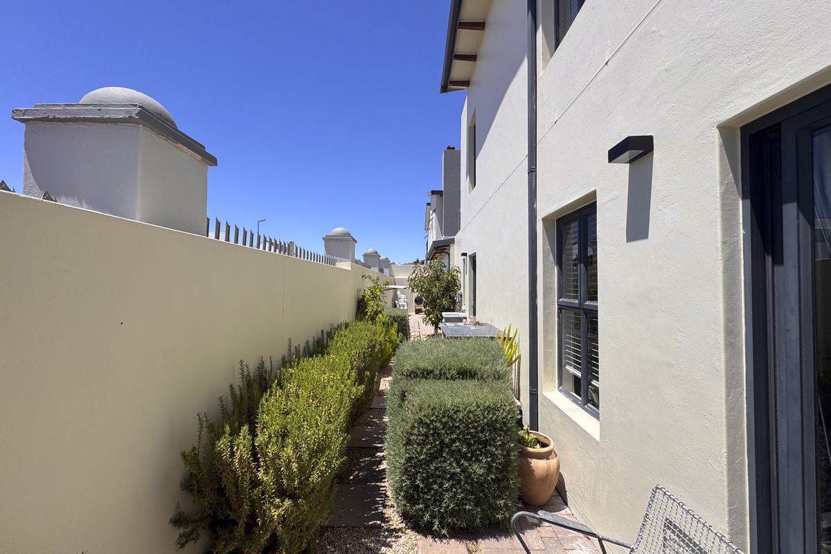 A side exterior walkway featuring a paved path, boundary wall with decorative pillars, and established garden hedging along the side of the house.