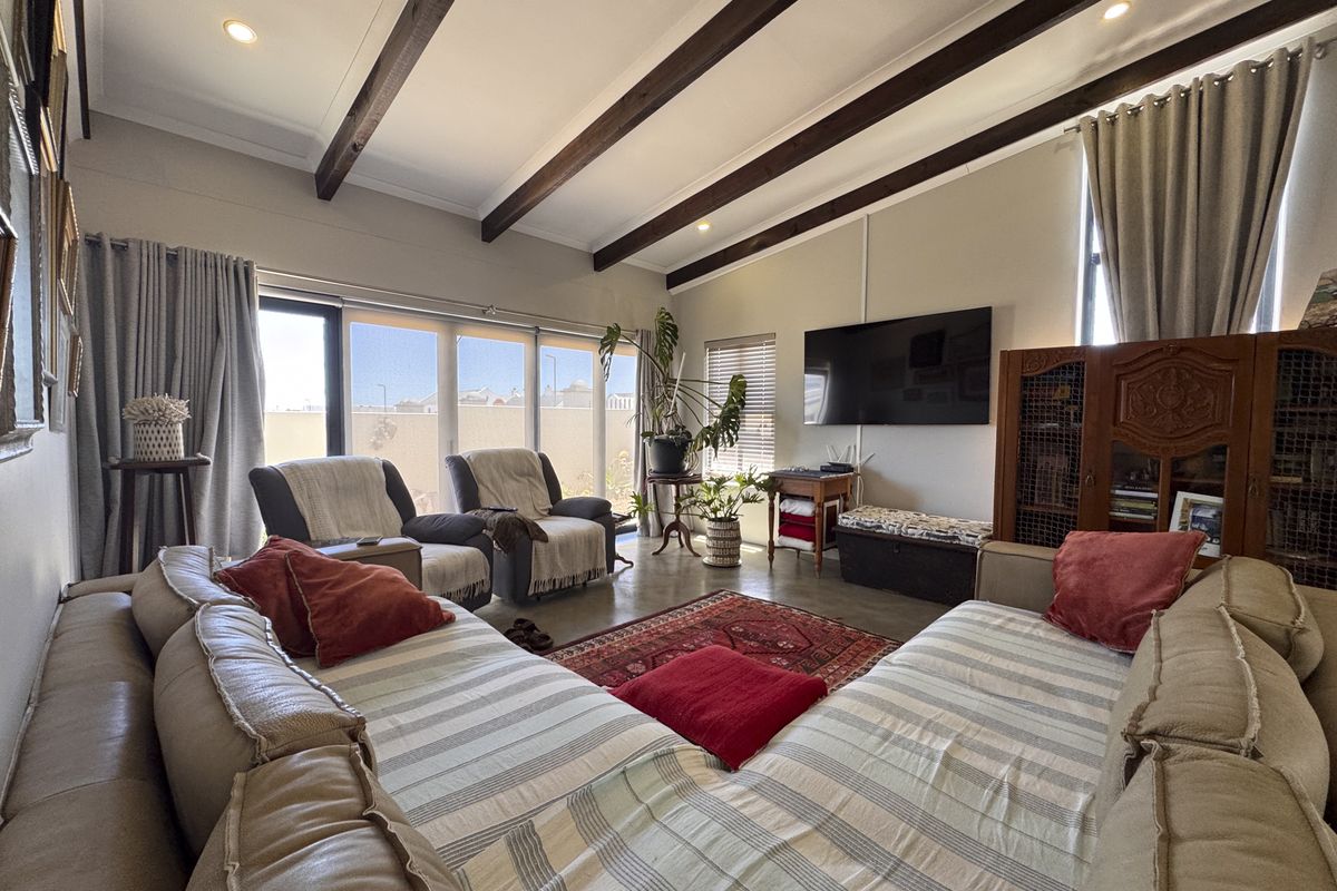 Spacious living room featuring exposed timber ceiling beams, polished concrete flooring, and large sliding glass doors providing ample natural light.